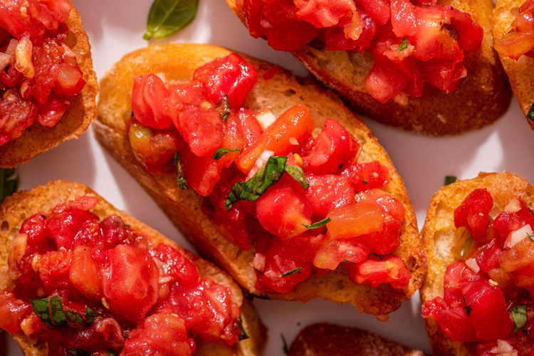 A top-down view of multiple bruschetta. The bruschetta is topped with tomatoes, garlic, and basil